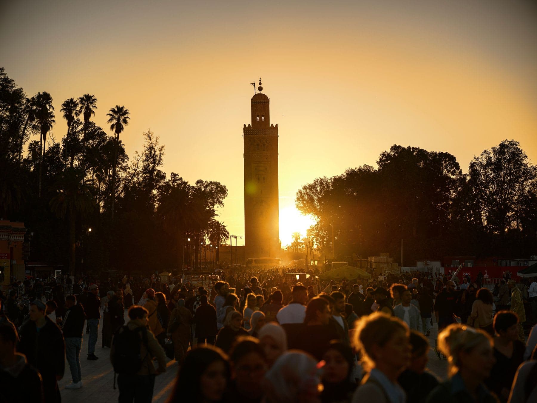 the Koutoubia Mosque minaret silhouetted against a golden sunset over the crowds of Jemaa el-Fnaa in Marrakech