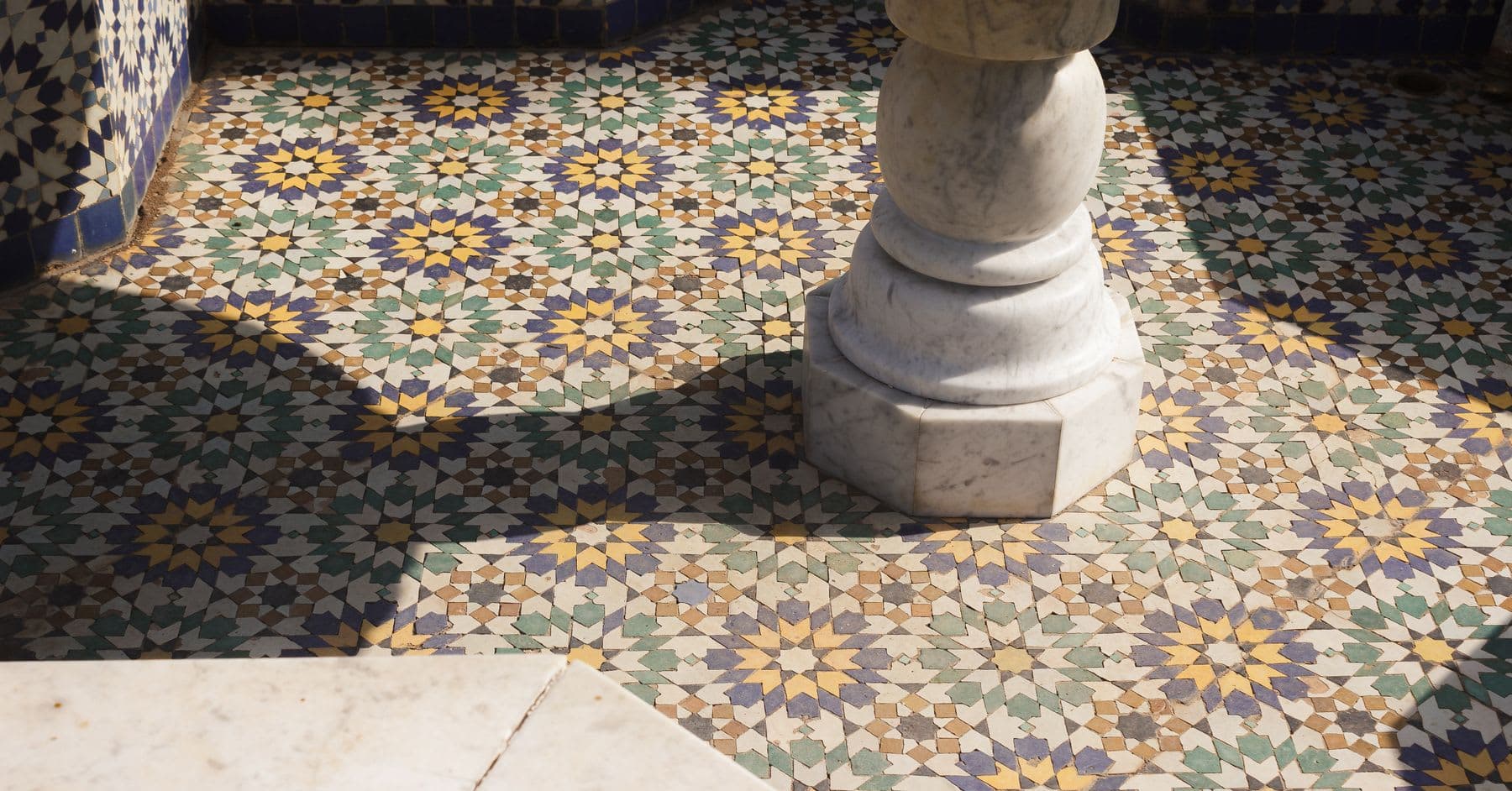 intricate hand-laid zellige mosaic tilework in gold, green, and indigo around a carved marble column base